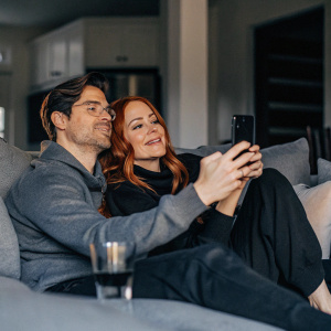 Amy Paffrath and Drew Seeley attending a virtual event for Just Dance 4. Wearing casual attire, they sit together in a cozy living room, framed by a blurred, homey background.