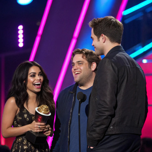 Vanessa Hudgens, Jonah Hill, and Robert Pattinson at the MTV Movie Awards. Neon pink and blue stage lighting. Vanessa holding an award, Jonah looks excited, Robert's back is turned.