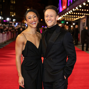 Karen Clifton and Kevin Clifton at premiere event, smiling widely. Karen in elegant black evening gown. Kevin in matching black suit. Vibrant red carpet with twinkling lights in the background.