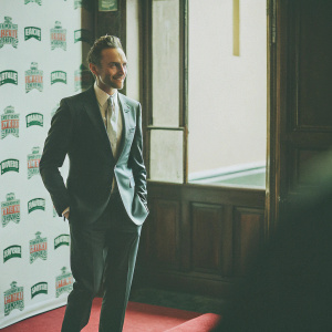 Tom Hiddleston, elegantly dressed in a dark suit with a light-colored tie, poses confidently. The backdrop features the Empire Film Awards logo and Jameson branding. The scene is set indoors with a red carpet.