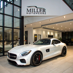 A sleek white Mercedes-Benz AMG GT S sports car showcased at a modern car dealership. Clean, minimalist setting with Miller Motorcars signage