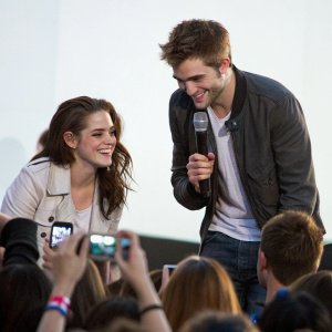 Kristen Stewart and Robert Pattinson at a fan meet and greet. Crowd of excited fans, brightly lit, casual interaction