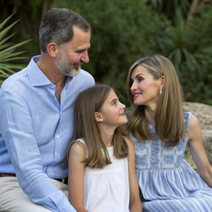 Casual family portrait: King Felipe of Spain, Queen Letizia, and their daughters Princess Leonor and Princess Sofia. Laid-back setting with greenery backdrop.
