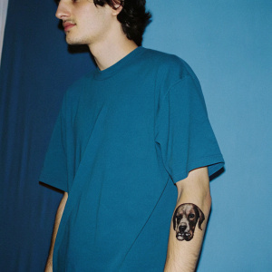 young man oversize T-shirt, arm with a realistic tattoo in black ink depicting a dog