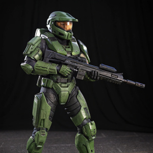 Digital 3D render of Master Chief in a green armor suit. Holding an assault rifle. Set against a black backdrop.