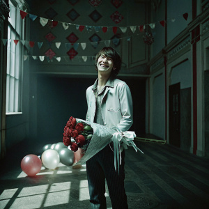 Akechi Goro from Persona 5, celebrating his birthday. He stands in a brightly decorated room filled with balloons and banners. He is holding a bouquet of red roses.