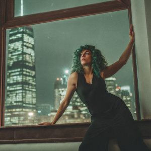 Sieria Wind, a character from One Punch Man, in a dramatic pose. She wears a black sleeveless dress and has green curly hair. The backdrop is a vibrant cityscape.