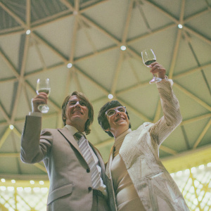 Cliff Richard and Cilla Black, both holding glasses of wine, posing amicably at a vintage music gala. Intricate ceiling design, soft lighting
