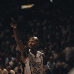 Ray Allen, basketball star, posing confidently. White Miami Heat jersey, number 34. Crowd blurred background