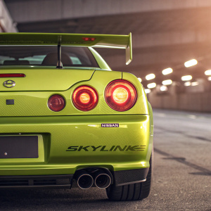 High-resolution digital art of a Nissan Skyline GT-R34. The car is lime green. The illustration focuses on the rear end, highlighting the taillights with a warm glow. The Nissan logo and 'Skyline' text are clearly visible.
