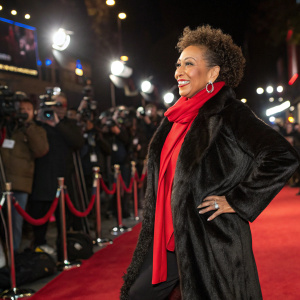 Tamara Tunie, wearing a black fur coat and red scarf, posing on the carpet at a movie premiere.