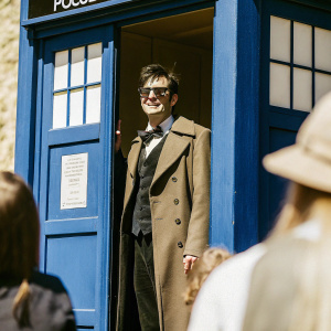 Tenth Doctor from Doctor Who standing in front of the TARDIS, a blue police box. Sci-fi convention with excited fans in the background.