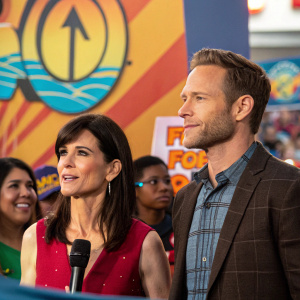 Perrey Reeves and Aaron Endress-Fox standing at a vibrant press conference. Lively background with bright logos and colors.