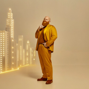 Flash Gordon in a futuristic setting. Bald head, well-groomed mustache, and full reddish-brown beard. Poses in front of a neon-lit cityscape.