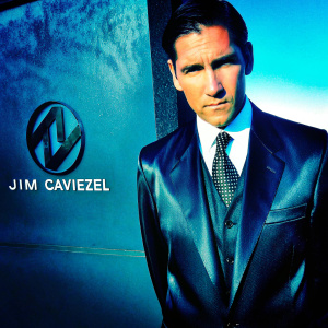 Jim Caviezel, middle-aged actor, in a sleek black suit and white shirt with a dotted pattern tie. Focused, serious expression. Dark, textured background with logo and text details. Close-up high resolution photo.