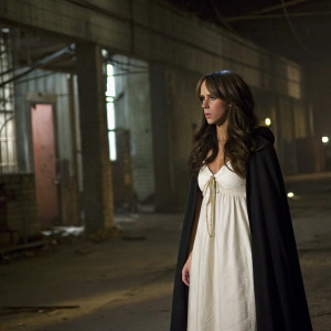 Jennifer Love Hewitt as Melinda on the set of 'Ghost Whisperer'. She's wearing a simple white dress and a dark cloak. Shot in a dimly lit, abandoned warehouse.