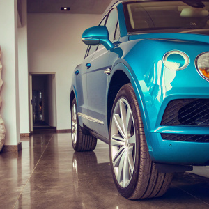 Blue Bentley Bentayga SUV displayed on polished concrete floor at luxury car dealership. Shiny wheels and sleek body