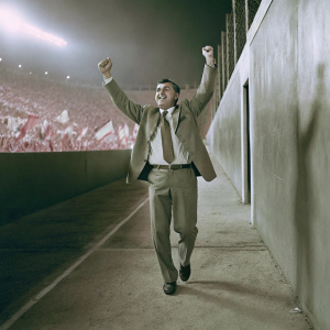 Carlo Ancelotti, in a formal suit and tie, celebrating victory on the sidelines. Stadium filled with cheering fans.