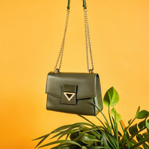 A close-up shot of the Furla Diva Shoulder Bag. Rich brown leather, gold chain straps. Geometric-shaped emblem. Feminine and modern design. White backdrop