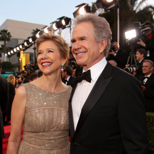 Warren Beatty and Annette Bening, smiling and posing at the Golden Globes ceremony. Crowd of photographers and formal attire everywhere.