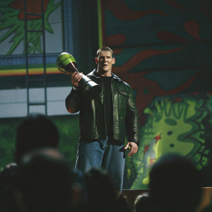 John Cena at Nickelodeon's Kids' Choice Awards. Intense expression, holding a large trophy amidst a backdrop filled with bright colors and animated designs.