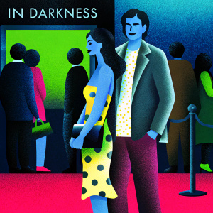 Emily Ratajkowski and Anthony Byrne at the 'In Darkness' film premiere. She's in a yellow and black polka-dot dress with a black clutch. He's in a patterned shirt and gray jacket. Crowded red carpet with promotional posters and fans.