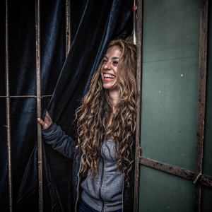 Shakira in a casual setting. Smiling warmly with long, curly hair. Green background.