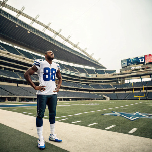 Dez Bryant, donning his Dallas Cowboys jersey number 88, stands confidently on an empty stadium field.