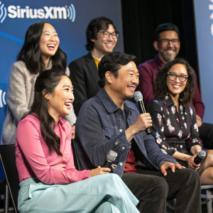 Group photo at SiriusXM event featuring Awkwafina, Jimmy O Yang, Constance Wu, Kevin Kwan, Henry Golding, Ken Jeong, and Michelle Yeoh. Relaxed, friendly demeanor, seated on stage with microphones, SiriusXM backdrop