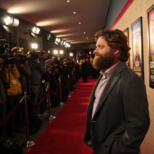 Zach Galifianakis, bearded actor, at a bustling premiere party. Red carpet, flashing cameras, movie posters displayed.