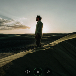 Jon Bellion's 'The Good In Me' album art. Male figure standing in sunset-lit desert. Warm golden glow, play button, music app elements.