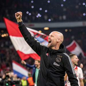 Erik Ten Hag, coach of AFC Ajax, celebrating a victory. Wearing club's training gear. Fans in background, waving flags.