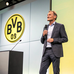 Hans-Joachim Watzke, CEO of Borussia Dortmund, standing in front of a sleek, modern backdrop at a Bundesliga press conference.