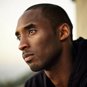 Close-up of Kobe Bryant's face. Neutral expression, dark skin tone. Background is blurred.
