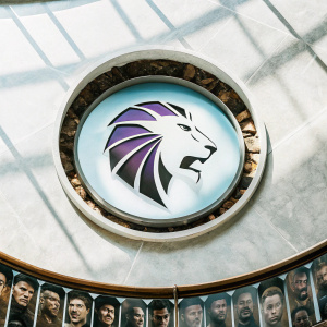 Digital artwork showcasing the LA Gladiators logo. Stylized lion's head with a backdrop featuring various faces. Predominantly purple color scheme.