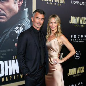Chad Stahelski and Heidi Moneymaker attending the premiere of John Wick: Chapter Two. Dark suit, elegant gown, promotional poster backdrop