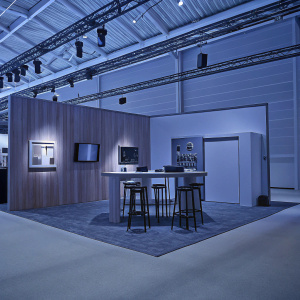 Modern trade show booth for Nokia. Sleek and professional design. Wooden panel backdrop, illuminated lighting fixtures, informational displays, central table with stools, showcasing Nokia's latest products and services.