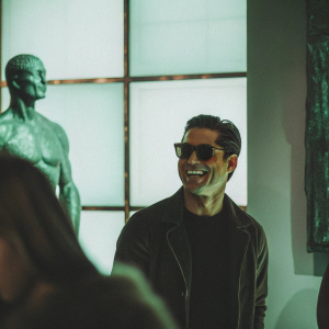 Mario Lopez, Hispanic actor, grinning in sunglasses. Modern art gallery backdrop.