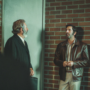 Donald Sutherland and David Schwimmer on set of 'Uprising'. Dark suit, beard, brick wall backdrop, leather jacket, striped shirt