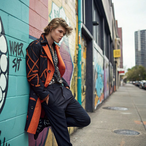 Jordan Barrett, wearing avant-garde outfit, posing against urban graffiti backdrop.
