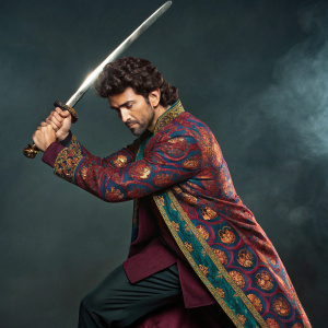 Hrithik Roshan, in a dynamic pose, wears a vibrant sherwani. He holds a gleaming sword. Dark, moody background.
