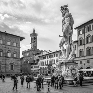 Gigantic Neptune statue towering over the tiny tourists in Florence, Italy. Crowded piazza with Renaissance architecture
