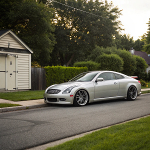 Silver Infiniti G35 Coupe parked in a quiet suburban street. Small storage shed in background.