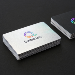 Business cards for 'Quantum Leap' featuring sleek silver and black design with holographic logo. Cards laid out in neat rows on matte black background.