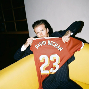 David Beckham at a charity event, donning a sharp navy suit. Poses with a Manchester United jersey featuring his name and number 23.