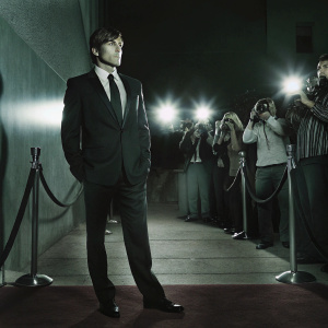 Zac Efron, wearing a formal black suit and tie, at the premiere of his latest film. Bright lights and paparazzi fill the red carpet scene.
