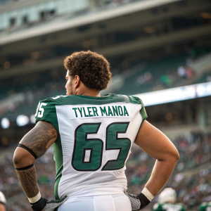 Tyler Manoa, football player, wearing green and white jersey, number 65. Short, curly hair. Stadium crowd in background