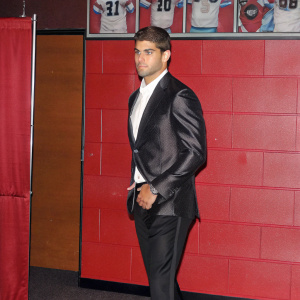 Jimmy Garoppolo, the quarterback of the San Francisco 49ers, in a sleek black suit. Attending a press conference. The backdrop is a wall filled with football memorabilia.