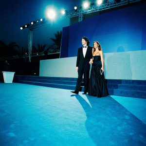 Eric Balfour and Erin Chiamulon, a glamorous couple, at a gala event. Formal attire, gray carpeted stage with bright lighting and logo backdrop.
