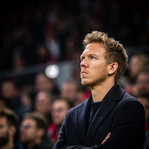 Julian Nagelsmann, intense gaze, in a dark blazer. Fuzzy crowd background at press conference